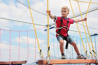 Brave blond hair kid playing rope course outdoor