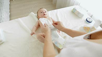 Young mother changing diapers to her 3 months old baby son lying on changing table