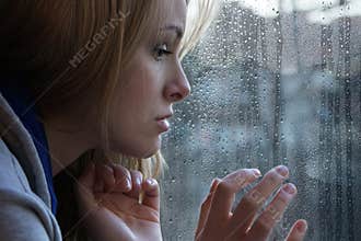 Sad young woman looking through window on rainy day