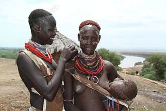 A young karo woman is painting the face of another woman carrying her child in her arms