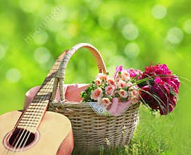 Romance, love, valentine`s day concept - wicker basket with bouquet of flowers, guitar on the grass