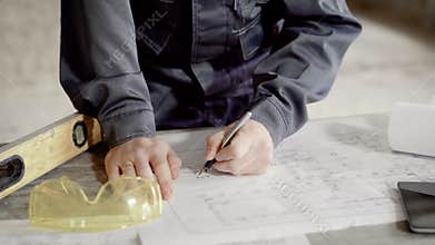 Close up shot of at the man`s hands, who makes notes in the construction drawing for the foreman and builders, the man