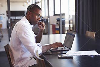 Young black man in wearing glasses using laptop in office