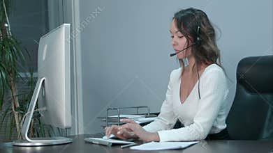 Friendly young asian female operator working on laptop with headset at modern office