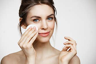 Cute beautiful natural brunette girl cleaning face with cotton sponge smiling looking at camera over white background