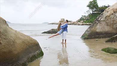 A man is circling a girl in his arms on a sea sandy beach. A pair of lovers swirl in slow motion