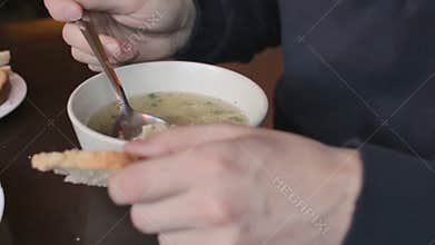 Young man eating tasty hot soup with bread at restaurant