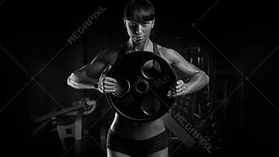 Black and white photo of fit power athletic confident young woman bodybuilder doing exercises with heavy weight barbell plate in