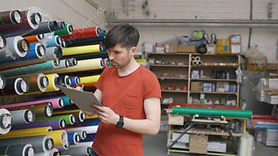Dolly shot of Young worker in warehouse with clipboard checking inventory. Man works in sales department of advertising