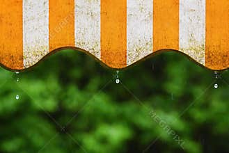 Rain. Awning on a balcony and drops of water on a natural colorful background during a spring day.
