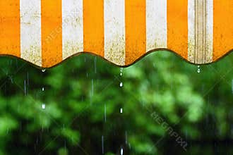 Rain. Awning on a balcony and drops of water on a natural colorful background during a spring day.