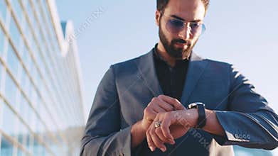 Young handsome man in a suit passing by the airport terminal and using smart watch. Modern devices, busy lifestyle