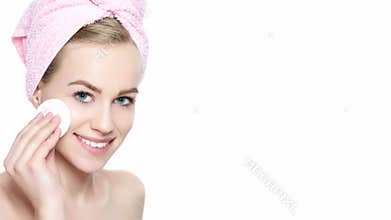 Smiling pretty girl with perfect complexion cleansing her face using soft cosmetic cotton pad