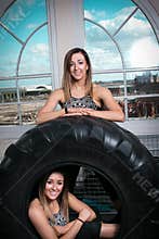 Two young smiling happy fitness women resting on a tyre