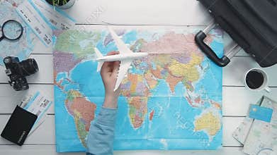 Travelling concept Top view traveler`s hand flying a toy airplane above the world map at white wooden desk