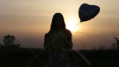 Pretty woman with heart shaped balloon at sunset