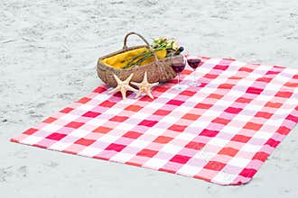 Picnic basket with glasses of red wine and starfishes on a blanket