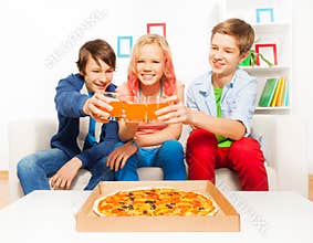 Positive teens holding glasses with juice on sofa