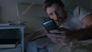 Young man in bed couch at home late at night using mobile phone in low light relaxed in communication technology