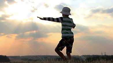 Boy prays to God, the boy raises his arms up and looking at the sky in a field