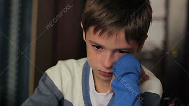 Little boy sitting at a desk crying, tears on his