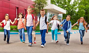 Row of happy kids with bags near school building