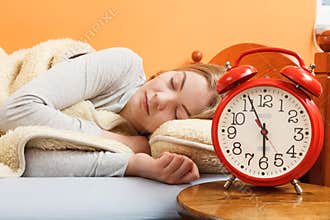Woman sleeping in bed with set alarm clock.