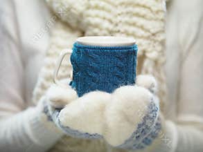 Woman hands in white and blue mittens holding a cozy knitted cup with hot cocoa, tea or coffee. Winter and Christmas time concept.