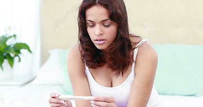 Woman sitting on bed holding pregnancy test