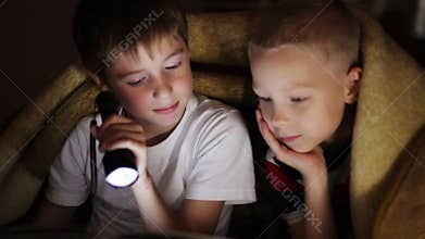 Two boys at night under a blanket reading a book