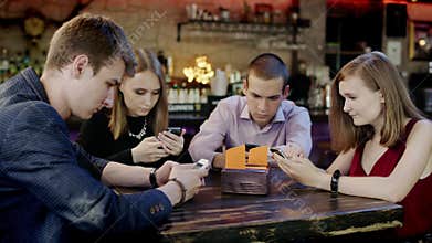 Company of young people is looking at their cellphones in the bar
