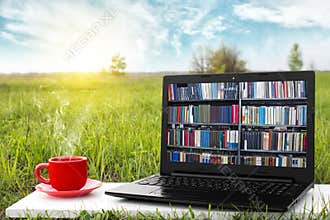 Laptop and cup of hot coffee on the background picturesque nature, outdoor office. E-book library concept. Internet books store.