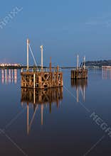 Two wooden boat jetty's, in the middle of a harbor, at night, reflecting in the very calm water