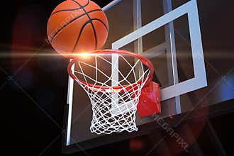 Basketball heading to the net at a sports arena with lens flare .