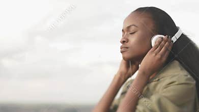 Lovely young african american woman listening music and relaxing on the blurred city background