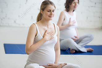 Pregnant young women doing prenatal yoga. Breathing exercises
