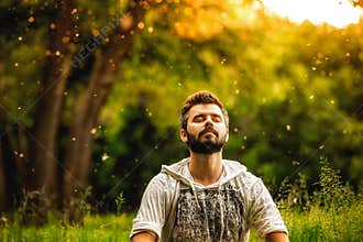 A bearded man is meditating on green grass in the park