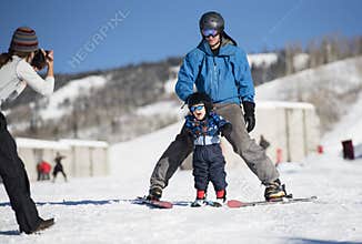 Toddler Screams with Delight as he Learns to Ski with Dad While Mom takes a Photo