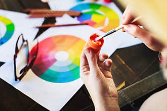 Woman`s hands holding paint, pencils and drawings on table