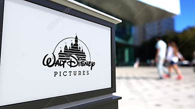 Street signage board with Walt Disney Pictures logo. Blurred office center and walking people background. Editorial 4K