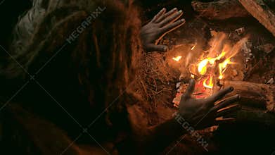 Neanderthal man warms his hands by the first bonfire in his cave