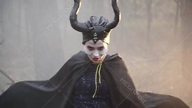 Closeup of a confused girl in the image of Maleficent in the misty forest