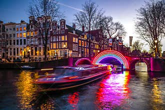 Cruise boats rush in night canals. Light installations on night canals of Amsterdam within Light Festival.