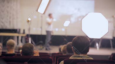 Unrecognizable public audience listening presentation. Speaker on the stage presenting products. Business traning