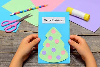 Child holding Christmas card in his hands. Paper greeting card with text Merry Christmas and Christmas tree with ornaments