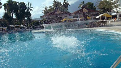 Beautiful young woman jumping into the swimming pool in hotel with splash of water.