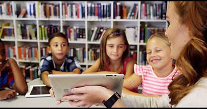 Teacher teaching school kids on digital tablet in library