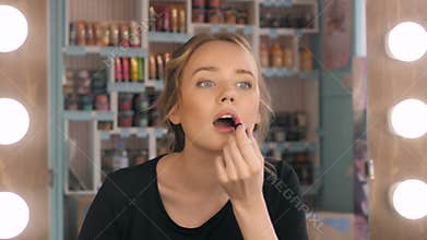 Woman putting red lipstick looking in mirror. Makeup at night getting ready before going to party.