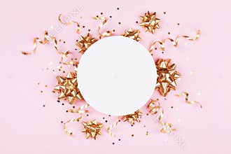Fashion mockup with golden bows, serpentine and star confetti on pink pastel table top view. Flat lay for birthday or christmas.