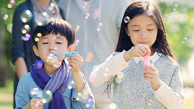 Two asian children blowing bubbles outdoors in park